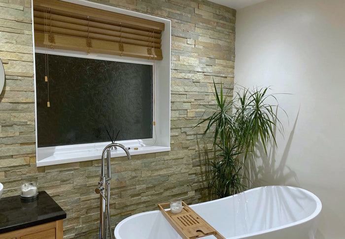 Minster Antiqued Limestone split face glacier cladding on a bathroom feature wall with indoor plant, wooden venetian blinds and deep white bathtub