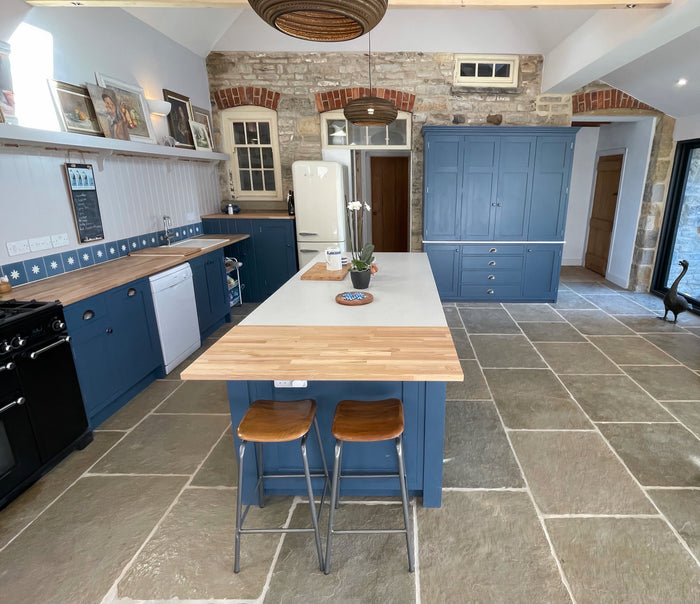 Natural Stone Online Minster Antiqued Limestone tile with navy blue kitchen cabinets and kitchen island with exposed brick wall