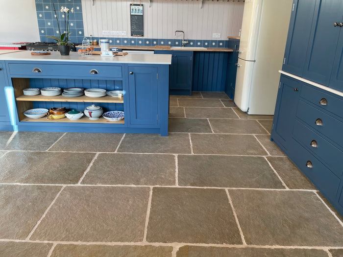 Natural Stone Online Minster Antiqued Limestone tile with navy blue kitchen cabinets and kitchen island with exposed brick wall and cream Smeg fridge